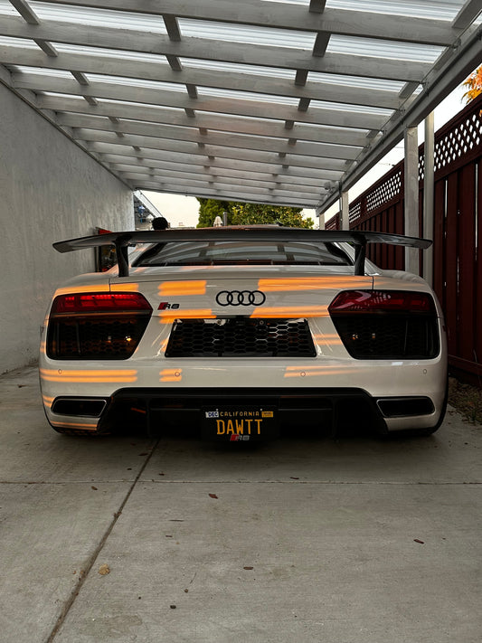 White Audi R8 rear view with custom spoiler and California plate in golden hour light.